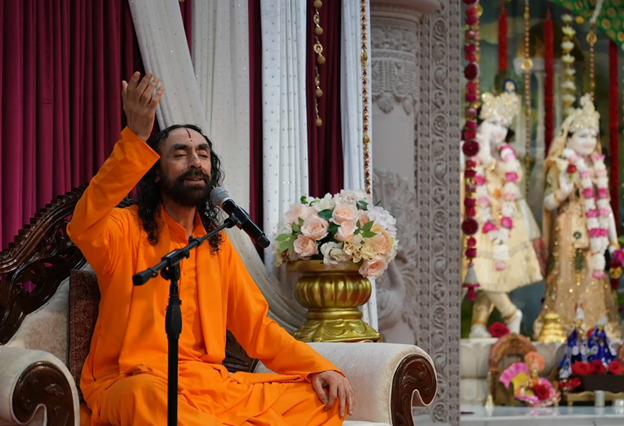 A person in an orange robe sitting on a chair with a microphone

AI-generated content may be incorrect.