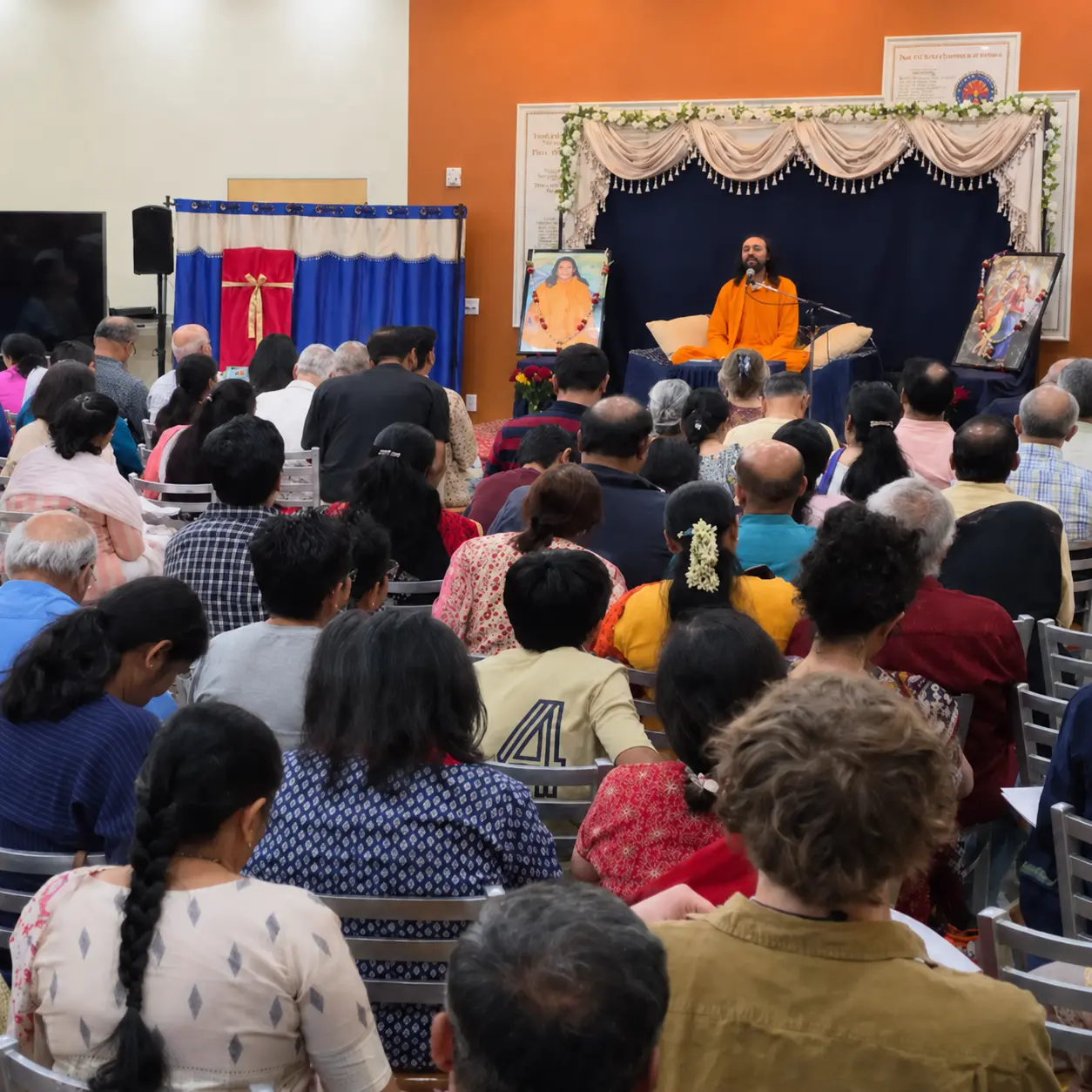 Swami Mukundananda sits on stage in saffron robes, speaking into a microphone before a large audience gathered for the Phoenix Life Transformation Program 2026.