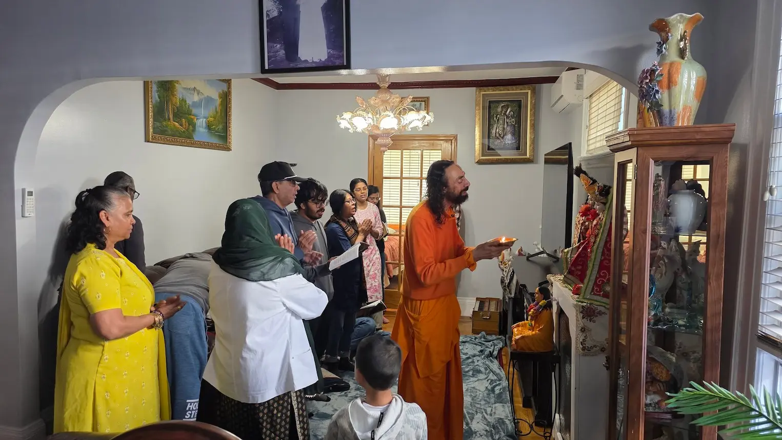 Swami Mukundananda performing aarti with devotees during a house satsang gathering in New York.