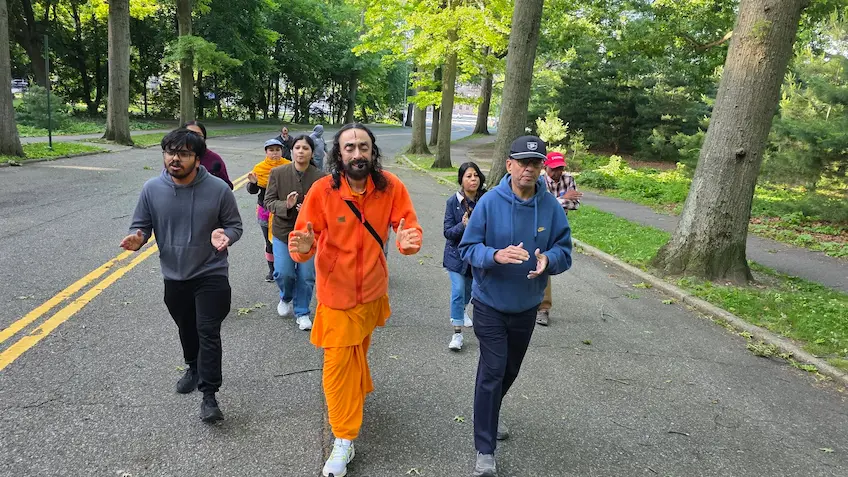 Swami Mukundananda walking with devotees, singing bhajans and sharing satsang during a morning walk.