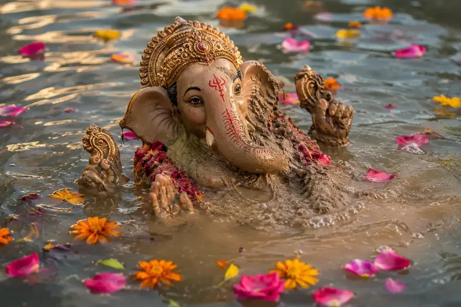 Ganesha partially dissolving in water, surrounded by colorful flower petals during Visarjan